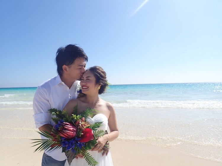 ビーチで南国のウエディングブーケを持っている新郎新婦