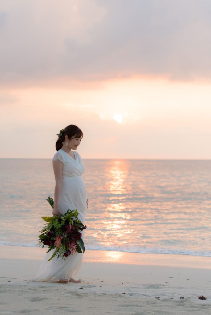 サンセットの海で、ウエディングドレスを着てたたずむ女性