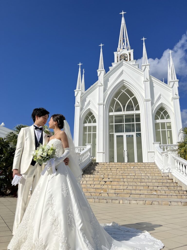 真っ白な教会の前に立つ新郎新婦