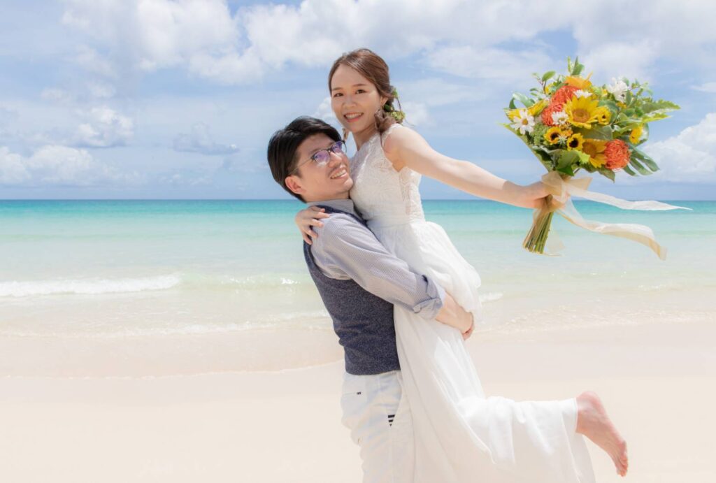 ビーチでウエディングブーケを持った新婦を抱き抱える新郎